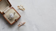 Oval engagement rings in white, yellow and rose gold beside a vintage ring box